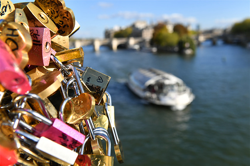 Paris, France-10 08 2022: Group of Love  locks hanging from a walkway overlooking  the Seine in Paris with a boat in the background, France.