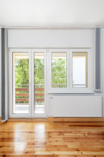 house room after renovation with open balcony door, new plastic pvc windows with white frame, installed vertical fabric blinds, heating radiator and wooden floor