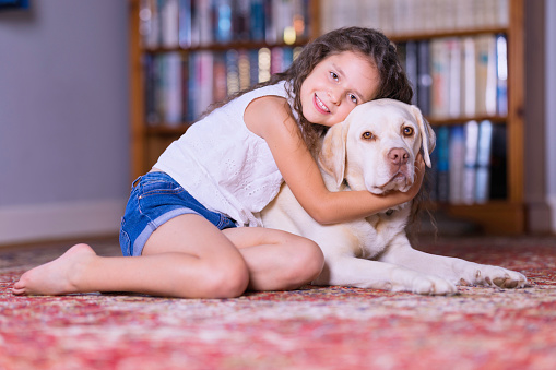 Young girl and her Labrador lying on the carpet. Focus on girl.