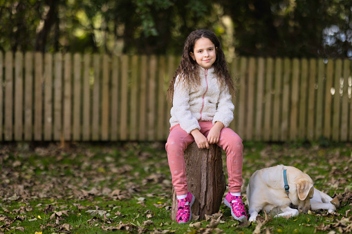 Eight-year-old brunette sitting on a log with her faithful dog.