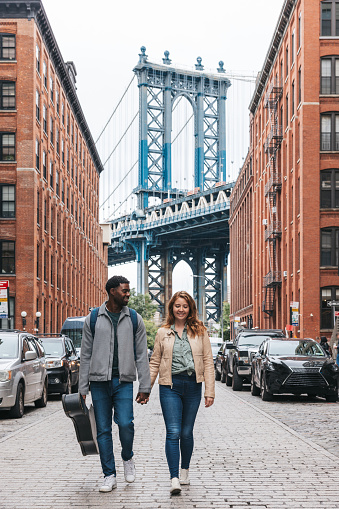 Happy mixed couple discovering New York City for the first time. They are walking in Dumbo next to Manhattan and Brooklyn Bridge.