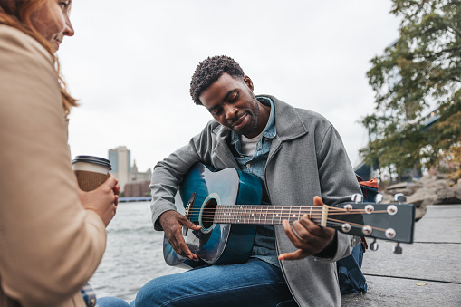 Affectionate couple play music down Brooklyn Bridge Park