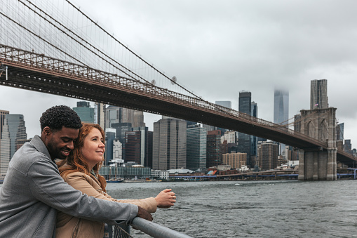 Couple enjoying a walk in Brooklyn Bridge Park next to the bridge and enjoying the amazing cityscape behind them.