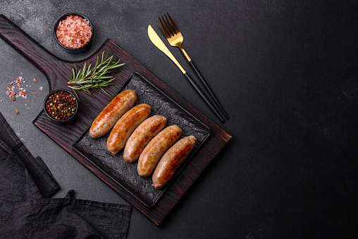 Tasty grilled sausages with spices and herbs on a black slate plate on a dark concrete background