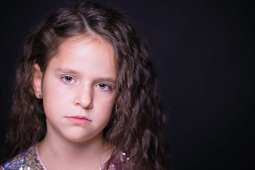 Close-up portrait of cute little child looking and pointing with fingers. Lovely dark curly hair. Sweet baby wearing colourful bracelets. Isolated on white background