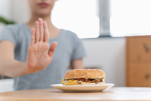 Unrecognize woman making hand sign to refuse unhealthy food on the table for dieting, Teenage girl refusing fast food, healthy eating and lose weight concept.