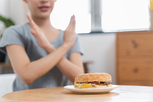 Portrait of young Asian woman making crossed arms hand sign to refuse junk food on the table for dieting, Teenage girl refusing unhealthy food, healthy eating and lose weight concept.