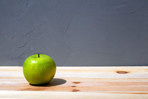 A fresh tasty raw green apple on a natural wood table with a rough concrete surface on a background with a copy space