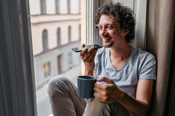 young man drinking coffee and sending a voice message indoors - vocoder imagens e fotografias de stock