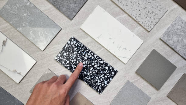 interior designer's hand selecting material samples palette contains various type, texture and color of artificial stones, marbles, grainy stone tiles, quartzs placed on grey travertine background. la paleta de muestras de materiales de selección de materiales del diseñador de interiores contiene varios tipos, texturas y colores de piedras artificiales, mármoles, azulejos de piedra granulados, cuarzos colocados sobre fondo de travertino gris.