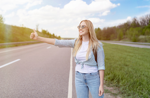 young woman hitchhiking while a car with a flat tire on the road is being repaired