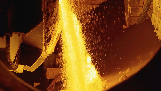 Molten raw materials in furnace. Stock footage. Close-up of bright molten substance pouring out in stream in industrial furnace.