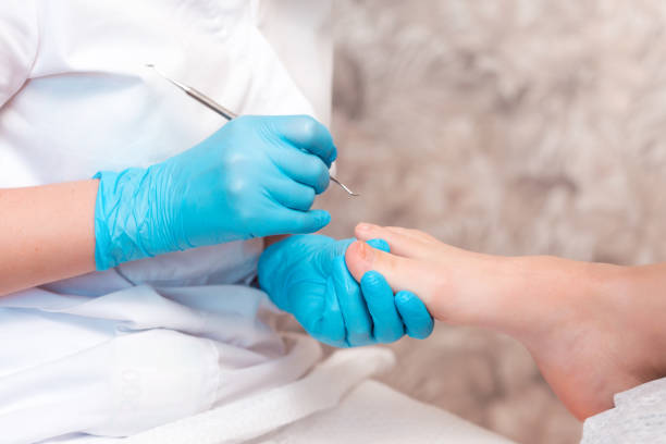 pedicurista hace una pedicura para el pie del cliente, limpiando las uñas con una cureta de doble cara. cerrar. el concepto de podología y podología - podiatrist customer service beauty spa fotografías e imágenes de stock