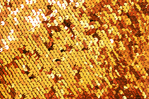Beautiful original festive background image of sparkling sequins in yellow, gold, orange colors. Fabric texture with shiny golden sequins.