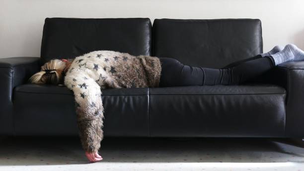 Exhaustion A senior woman lies on her stomach on the sofa with the left arm hanging down to the floor long covid stock pictures, royalty-free photos & images