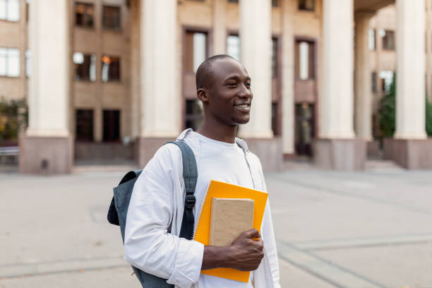 istock Smiling african american male student with backpack and workbooks posing over college building background 1434199491