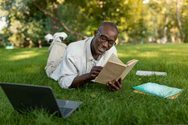 istock Happy black student guy in eyeglasses reading book, preparing for exams and enjoying studying outdoors in park 1434200648