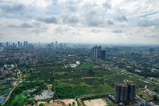 aerial drone shot over gurgaon showing monsoon clouds with light rays falling on ground crowded with homes houses, sohna highway feilds and water pools around under construction buildings and architecture