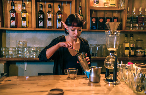 Young woman barista with elf ears preparing ice coffee at café