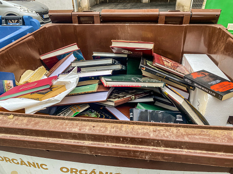 Valencia, Spain - October 9, 2022: Lots of books inside garbage container in the street. Having the chance of find information online people don't want to keep encyclopedias taking out space in their bookshelves