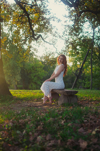 Young woman posing on the bench by the tree