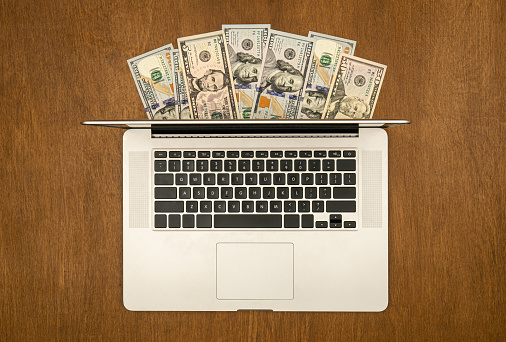 Laptop and dollar bills on wooden background, flat lay, concept of freelancing, remote work, work online and work from home.