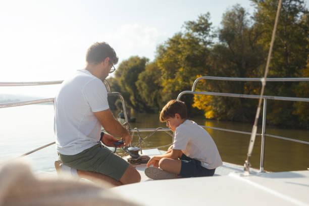 junger kaukasischer vater, der seinem sohn das binden von segelknoten beibringt - sailing nautical vessel family lake stock-fotos und bilder