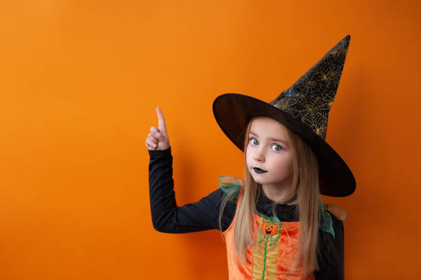 istock Happy Halloween! Cute little witch points her finger at the copy space 1434210574