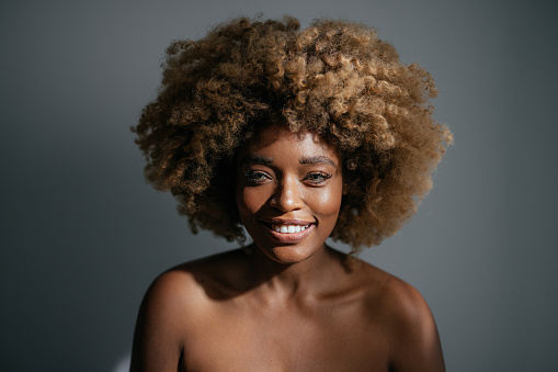 Studio shot of beautiful African-American woman with clean skin and curly hair looking at camera and smiling.