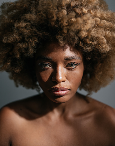 Studio shot of  serious African-American woman with clean skin and curly hair looking at camera.