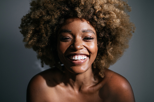 Studio shot of beautiful African-American woman with clean skin and curly hair looking at camera and laughing.