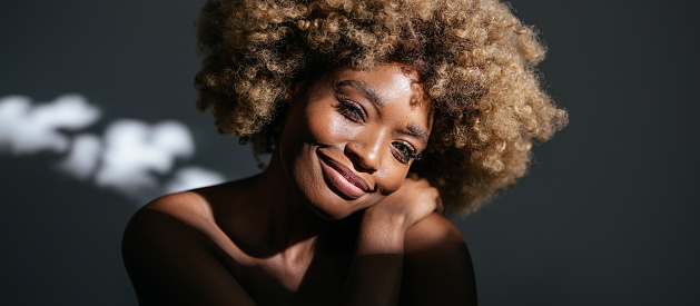Studio shot of African-American woman with clean skin and curly hair looking at camera and smiling.