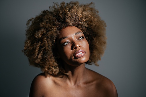 Studio shot of smiling African-American woman with clean skin and curly hair looking away.