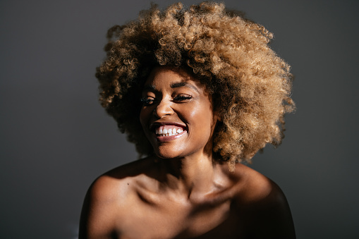 Studio shot of beautiful African-American woman with clean skin and curly hair laughing.