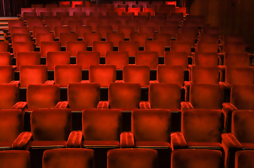 Red velvet chairs in a theater, highlighting the symmetry, lines and repetition of the seats.