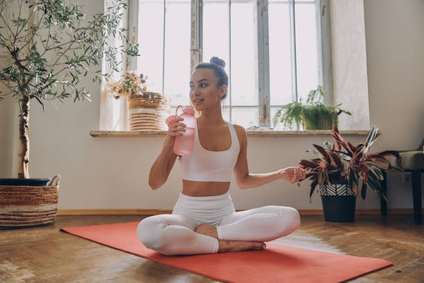 istock Beautiful young woman drinking water after training while sitting on the exercise mat at home 1434213944