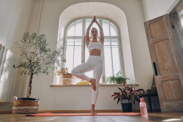 istock Beautiful young woman looking concentrated while practicing yoga in front of the window at home 1434214480