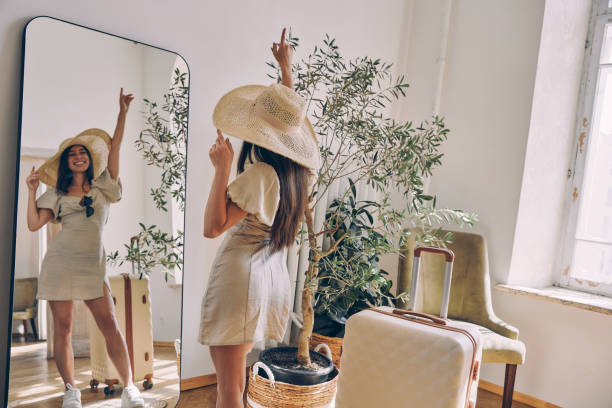 집에서 거울 앞에 서있는 동안 모자를 쓰고 팔을 뻗은 아름다운 여자 - mirror women dress looking 뉴스 사진 이미지