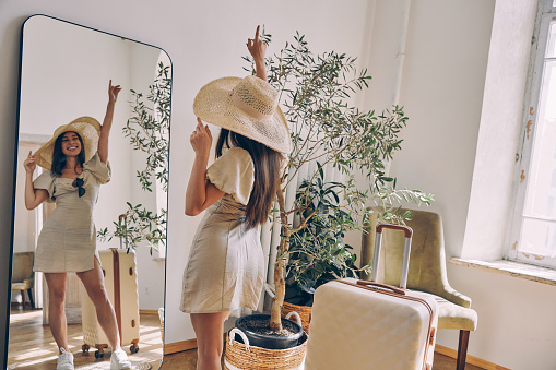 Beautiful woman wearing hat and keeping arm outstretched while standing in front of the mirror at home