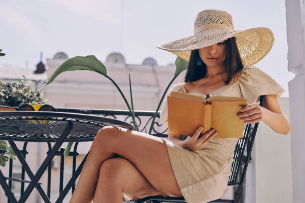 istock Beautiful young woman in elegant hat reading book while relaxing on the balcony 1434214945