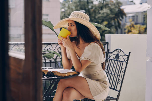 istock Attractive young woman in elegant hat drinking coffee while relaxing on the balcony 1434215067