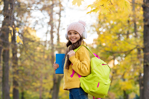 kid listen music in autumn park. fall is a time for study. back to school. concept of online education. child carry books for study. girl in earphones with school bag.
