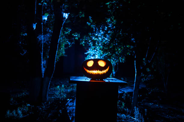 istock Pumpkin Burning In Forest At Night - Halloween Background. Scary Jack o Lantern smiling and glowing pumpkin with dark toned foggy background. Selective focus 1434216191