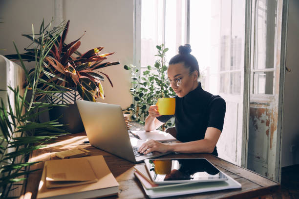 Confident woman using laptop and enjoying hot drink while sitting at her working place in office