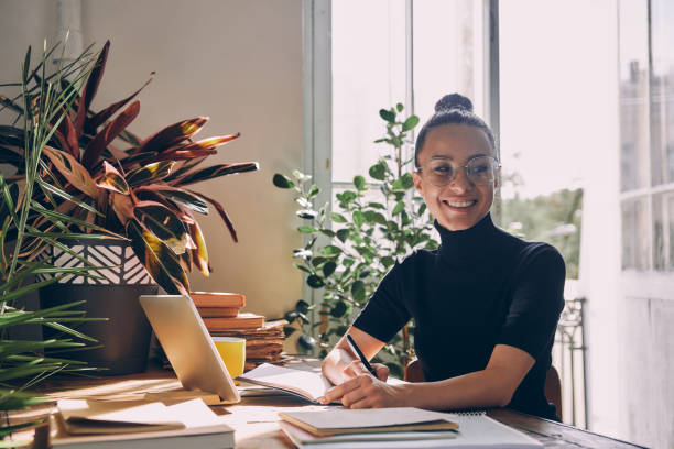 istock Attractive young woman making notes and smiling while sitting at her working place in office 1434218668