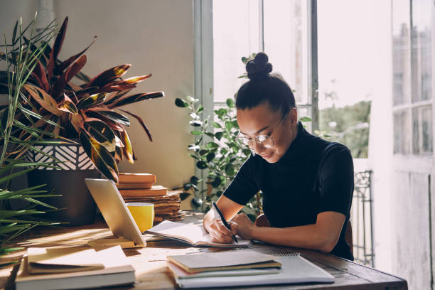 istock Beautiful young woman making notes and smiling while sitting at her working place in office 1434218670