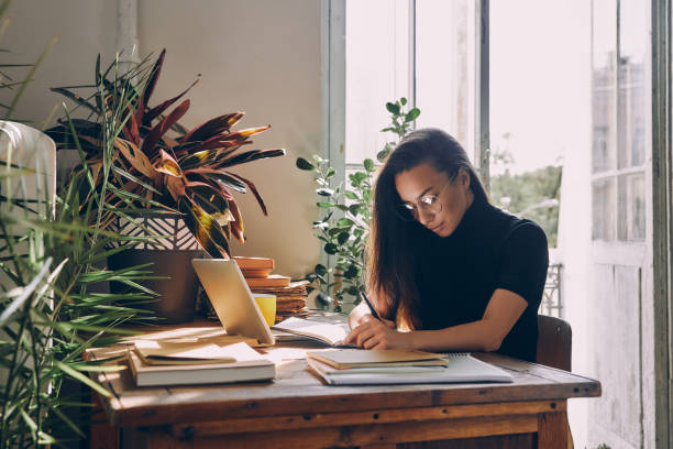 istock Concentrated young woman sitting at the table and making notes while working from home 1434218758