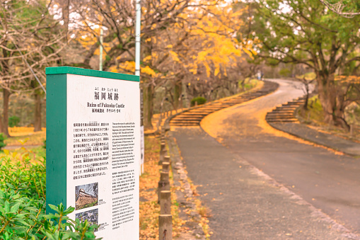 kyushu, fukuoka - dec 06 2021: Information panel in front of the Matsunoki-zaka slope covered by autumn leaves about the history of the ruins of Fukuoka castle designated as national historic site.