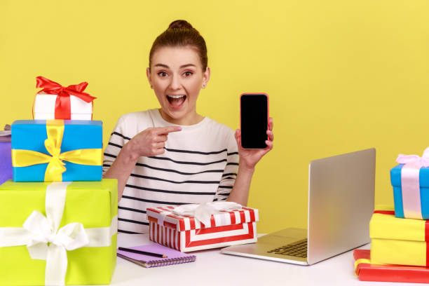 istock Woman with gift boxes and pointing at cell phone with blank display, empty mock up screen. 1434250878