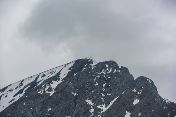 istock Monochrome scenery with high mountain peak with snow cornice in gray cloudy sky at overcast. Dark atmospheric mountain landscape with large pinnacle in lead gray sky at rainy weather in grayscale. 1434262878